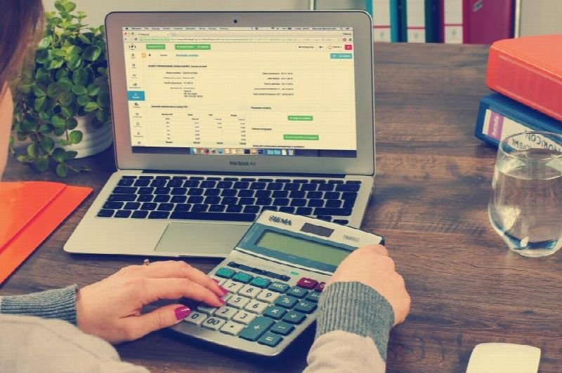 Hands using a calculator next to a laptop showing a spreadsheet