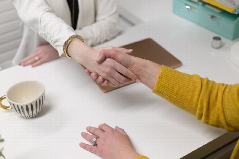 Two people shaking hands across a desk during a consultation