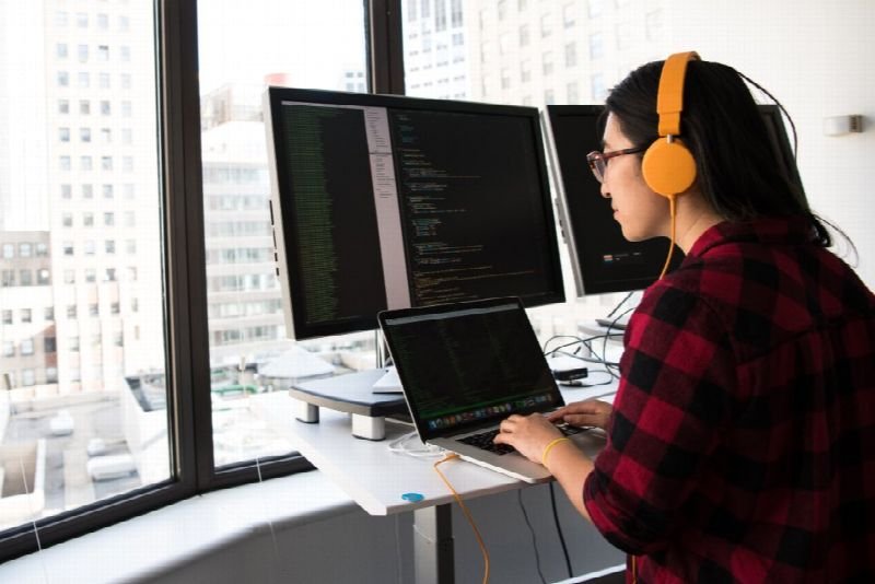 Developer wearing headphones writing code across multiple monitors