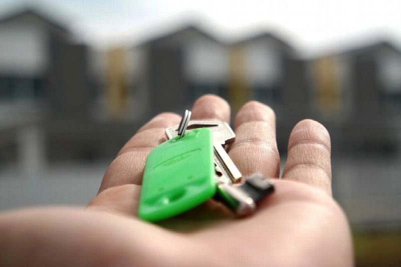 Hand holding a set of house keys outside a residential building