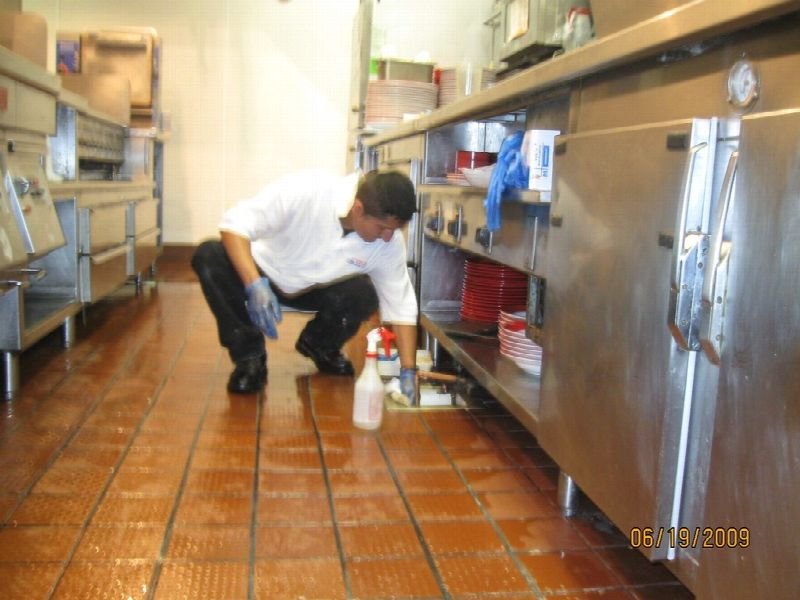 Worker kneeling to clean the floor of a commercial kitchen