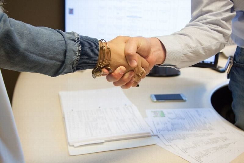 Two people shaking hands over paperwork at a desk