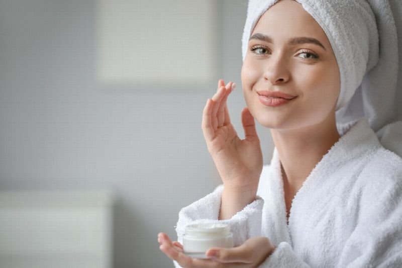 Woman in a robe and towel applying skincare cream
