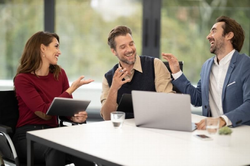 Three coworkers laughing during a conversation at a meeting table