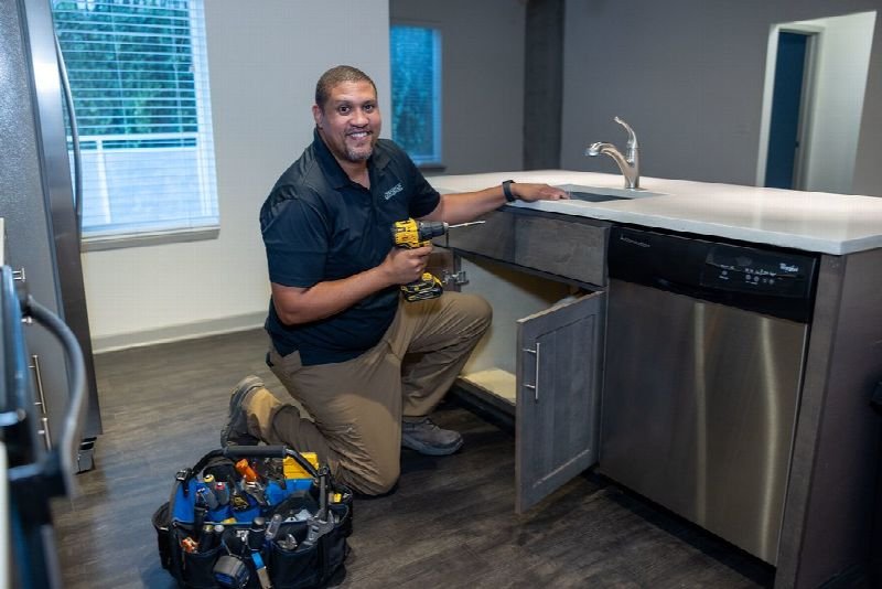 Technician kneeling to repair an appliance in a residential kitchen